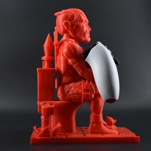 Peut inclure: Une figurine rouge en 3D imprim&eacute;e d'un personnage assis sur des toilettes tenant une manette de jeu vid&eacute;o blanche. La figurine est sur une base rouge avec une &eacute;p&eacute;e et d'autres d&eacute;tails.