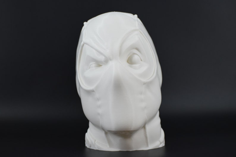May include: White 3D printed bust of a masked superhero head. The mask has a detailed design with a prominent nose and eye holes.