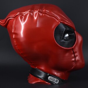 May include: A red and black Deadpool mask with a detailed design. The mask is made of a shiny material and has a black eye hole.