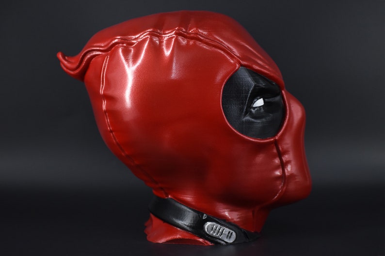 May include: A red and black Deadpool mask with a detailed design. The mask is made of a shiny material and has a black eye hole.