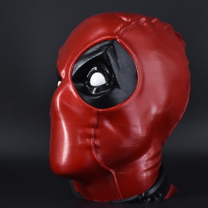 May include: A red and black Deadpool mask with a white eye. The mask is made of a smooth, shiny material.