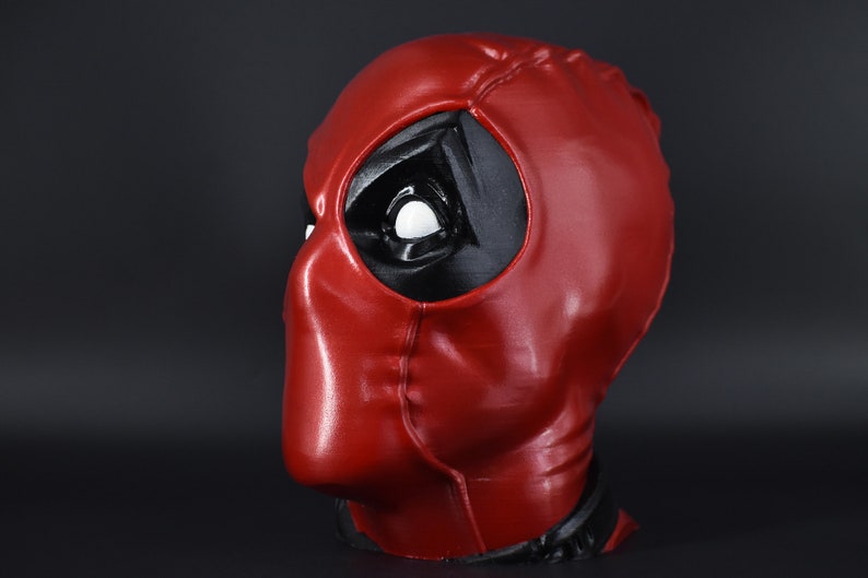 May include: A red and black Deadpool mask with a white eye. The mask is made of a smooth, shiny material.