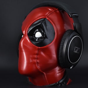 May include: A black over-ear headphone with a red and black Deadpool mask on a black background.