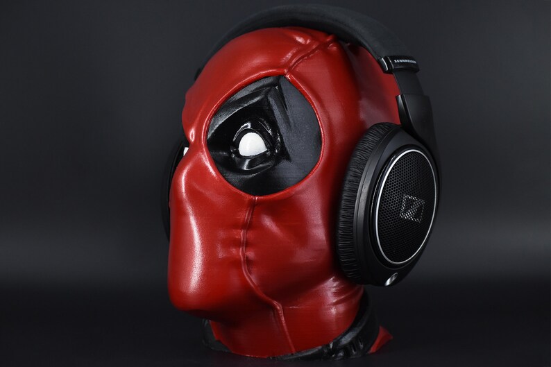 May include: A black over-ear headphone with a red and black Deadpool mask on a black background.