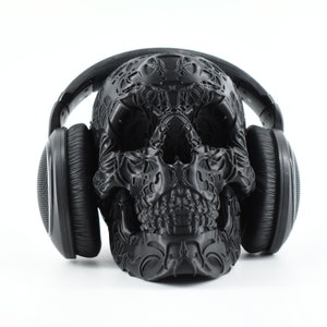 May include: A black skull with intricate details is wearing a pair of black headphones.