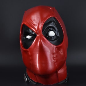 May include: A red and black Deadpool mask with a white eye. The mask is made of a smooth, shiny material.