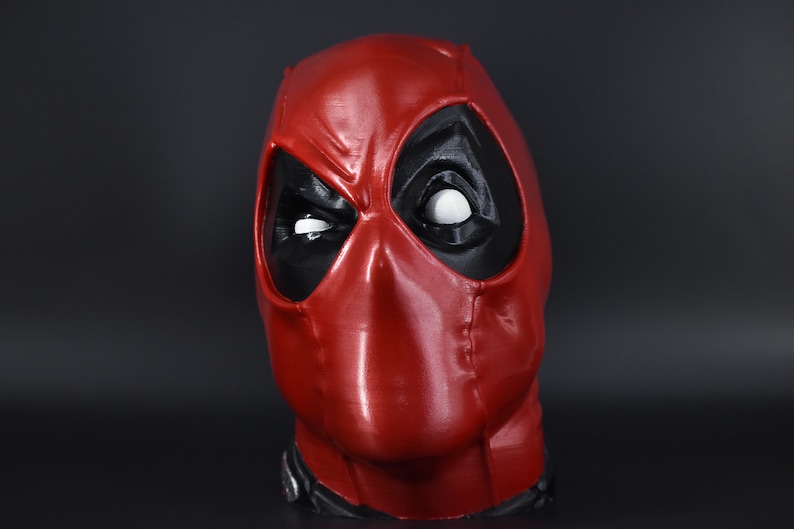 May include: A red and black Deadpool mask with a white eye. The mask is made of a smooth, shiny material.