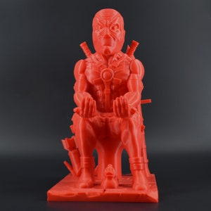 Peut inclure: Une figurine rouge de Deadpool imprim&eacute;e en 3D assise sur un tr&ocirc;ne avec un canard en caoutchouc &agrave; ses pieds.