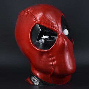 May include: A red and black Deadpool mask with white eyes. The mask is made of plastic and has a glossy finish.