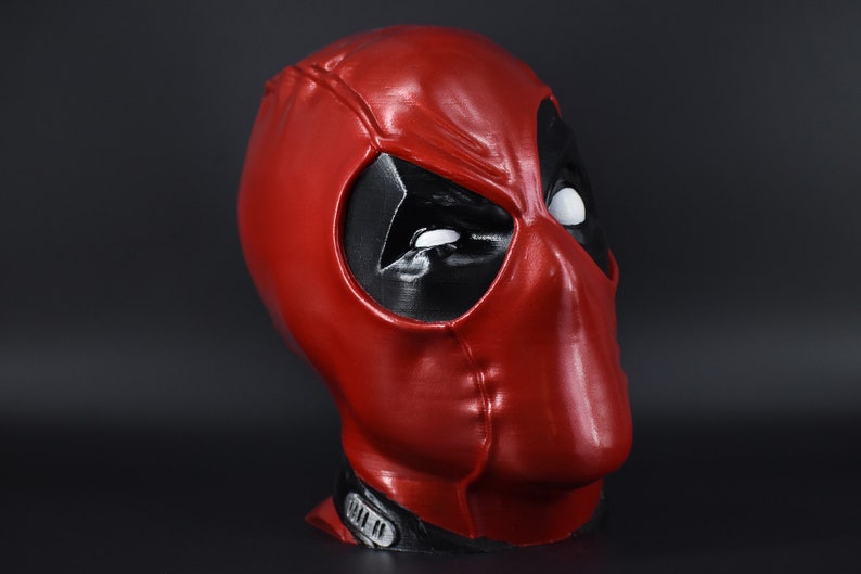 May include: A red and black Deadpool mask with white eyes. The mask is made of plastic and has a glossy finish.