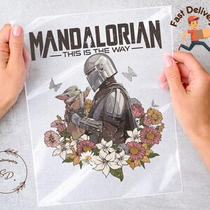 May include: A clear plastic sheet featuring a graphic of The Mandalorian and Grogu surrounded by flowers. The text "MANDALORIAN - THIS IS THE WAY" is at the top. The image includes butterflies and a floral arrangement.