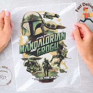 May include: A clear plastic sheet featuring a Star Wars design with the text "The Mandalorian and Grogu." The design includes images of the Mandalorian, Grogu, and other characters in shades of green, brown, and beige. The phrase "This is the Way" is also included.