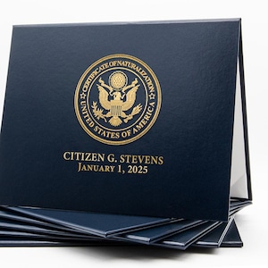 May include: A stack of navy blue document holders. The top holder displays a gold emblem and text: "CERTIFICATE OF NATURALIZATION UNITED STATES OF AMERICA" and "CITIZEN G. STEVENS JANUARY 1, 2025".