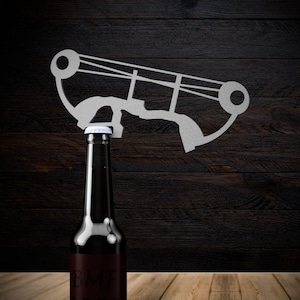 May include: A dark brown glass bottle with a white label that says "BMF BEER" on a wooden surface. A white metal bottle opener is above the bottle.