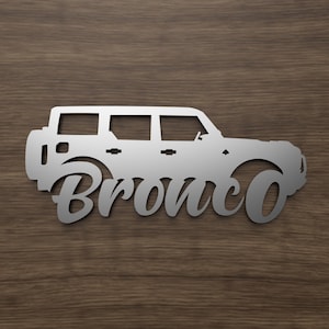 May include: A silver metal silhouette of a Ford Bronco with the word "Bronco" written in a stylized font below the vehicle.