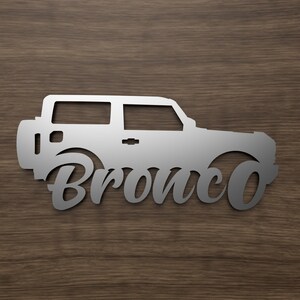 May include: A silver metal silhouette of a Ford Bronco with the word "Bronco" in a stylized font below the vehicle.