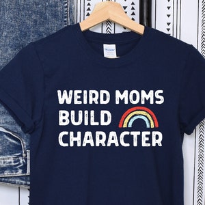 May include: A navy blue t-shirt with the text "Weird Moms Build Character" and a rainbow graphic.