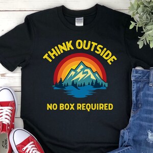 May include: Black t-shirt with a retro-style mountain scene and the text "Think Outside No Box Required".