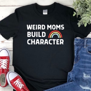May include: Black t-shirt with white text that reads "Weird Moms Build Character" with a rainbow graphic.