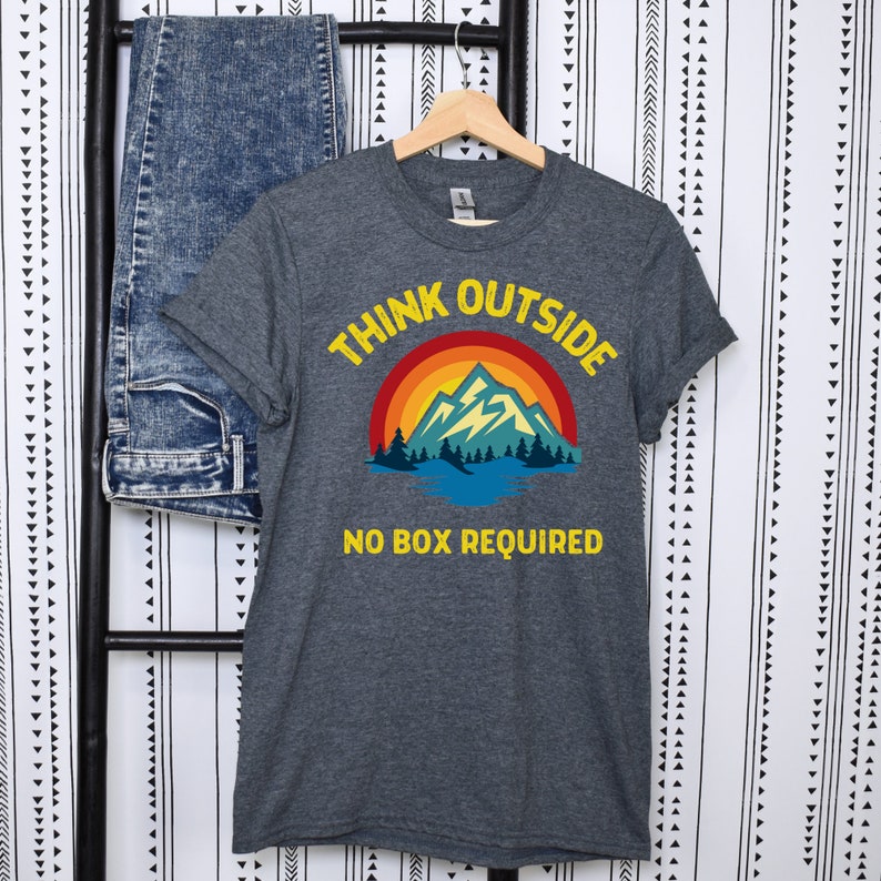May include: A dark heather grey t-shirt with a retro mountain scene and the text "Think Outside No Box Required".