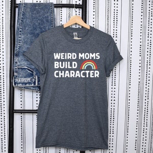 May include: A dark heather grey t-shirt with the text "Weird Moms Build Character" in white with a rainbow graphic.