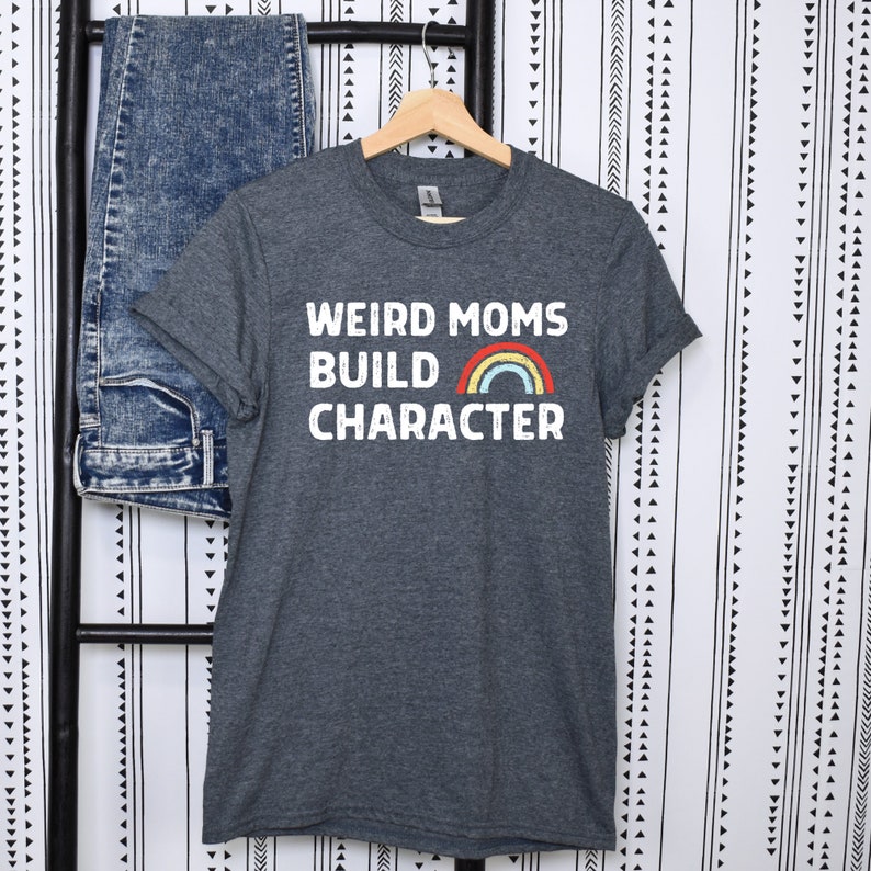 May include: A dark heather grey t-shirt with the text "Weird Moms Build Character" in white with a rainbow graphic.