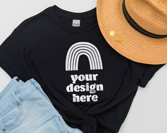 Puede incluir: Una camiseta negra de manga corta con un gráfico blanco de un arcoíris y el texto "your design here" en letras blancas, acompañada de un sombrero de paja beige con una banda negra y unos vaqueros de mezclilla azul claro.