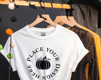 May include: A white short-sleeved t-shirt featuring a black graphic print on the chest. The design consists of a central pumpkin illustration surrounded by the circular text "PLACE YOUR DESIGN HERE" in a bold, black, serif typeface.