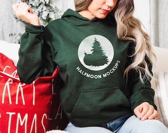 Puede incluir: Una sudadera con capucha de color verde oscuro que presenta un gráfico circular blanco en el pecho. El gráfico muestra un pino y un adorno redondo con el texto HALFMOON MOCKUPS impreso en letras mayúsculas blancas bajo el diseño circular.