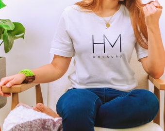 May include: A white short-sleeved t-shirt featuring the black text HM MOCKUPS printed on the chest. The shirt is paired with dark blue denim jeans. A gold-toned necklace with a small pendant is worn around the neck, and a bright green bracelet is visible.