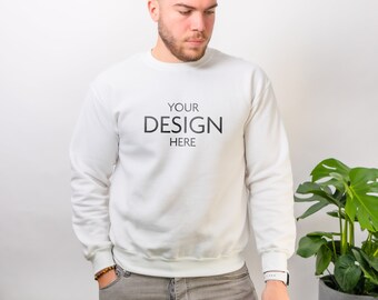 May include: A white long-sleeve crewneck sweatshirt featuring the black text "YOUR DESIGN HERE" printed on the center of the chest. The garment has a ribbed neckline, cuffs, and hem, providing a clean and simple look for casual wear.