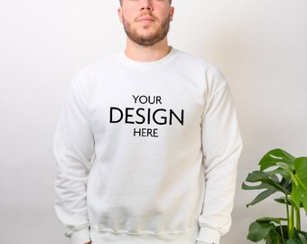 May include: A plain white long-sleeve crewneck sweatshirt featuring the black text "YOUR DESIGN HERE" printed on the center of the chest. The garment has a ribbed neckline, cuffs, and hem, providing a clean and simple look for custom graphics.