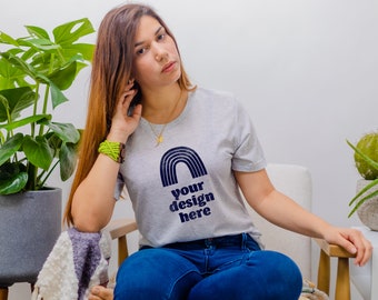 May include: A light gray short-sleeve t-shirt featuring a dark blue graphic of a rainbow arch above the text "your design here" printed in a bold, sans-serif font. The shirt is paired with dark blue denim jeans.