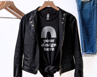 May include: A black t-shirt featuring a silver rainbow graphic and the text "your design here" in silver lettering, layered under a black jacket with quilted side panels and a metal zipper, displayed alongside a pair of distressed blue jeans.
