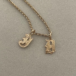 May include: A gold chain necklace with two gold charms, each featuring a stylised letter 'J' in an old English font.