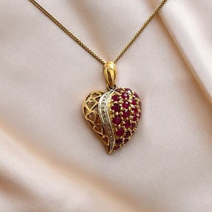 Puede incluir: Un collar de oro con un colgante en forma de corazón con un diseño de rubí rojo y diamante blanco.