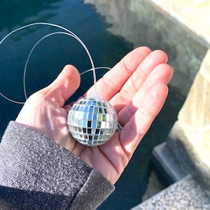 May include: A silver disco ball ornament hanging from a thin white string. The ornament is about 2 inches in diameter and has a mirrored surface.