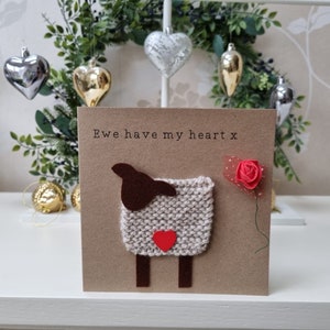 May include: A brown card with the text "Ewe have my heart x" and a knitted sheep with a red heart on its chest. A red rose with a green stem is on the right side of the card.