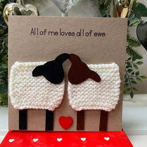 May include: A handmade card with a brown background featuring two white sheep with black and brown faces. The sheep are kissing and there is a red heart between them. The card says "All of me loves all of ewe".