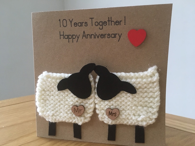 May include: A handmade card with a knitted sheep design. The card says "10 Years Together! Happy Anniversary" and has a red heart and two wooden hearts that say "Mr." and "Mrs."