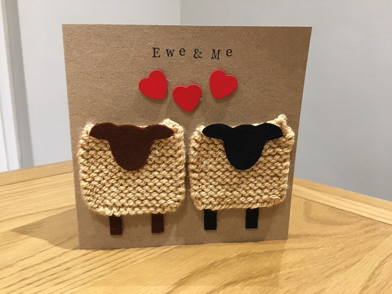 May include: A handmade card with the text "Ewe & Me" and three red hearts. The card features two knitted sheep, one brown and one black, with felt faces.