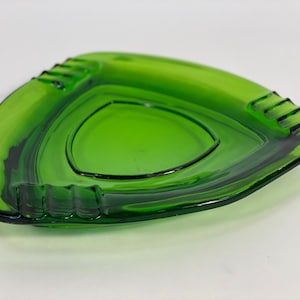 May include: A green glass ashtray shaped like a triangle with three indentations on each side.