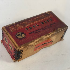 May include: A vintage cardboard box with a red label that reads "TOOL BITS" and "VANADIUM-ALLOYS STEEL COMPANY". The box is labeled with the size "12 3/16".