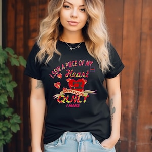 Peut inclure: T-shirt noir avec l'inscription "I sew a piece of my heart into every quilt I make". Le motif comprend un cœur rouge et des accents colorés. Le t-shirt est porté avec un jean bleu.
