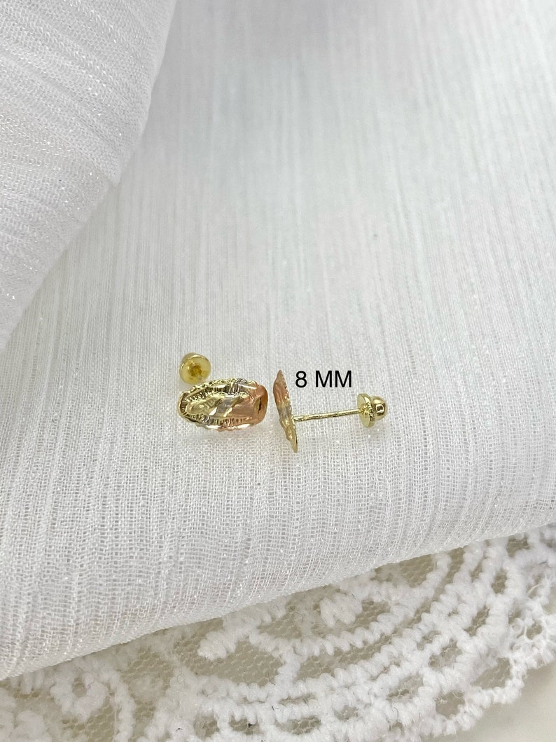 Op de afbeelding: Een paar gouden oorstekers. E&eacute;n oorbel heeft een ovale vorm met een textuurontwerp en driekleurig goud. De andere oorbel is een pin met een kleine ronde stud. De tekst "8 MM" is zichtbaar.