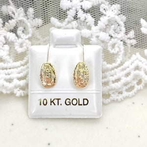 Op de afbeelding: Een paar goudkleurige oorstekers met een gedetailleerd ontwerp, gepresenteerd op een witte standaard. De oorbellen zijn gemarkeerd met "10 KT. GOLD". De achtergrond is een wit oppervlak met een kantpatroon.