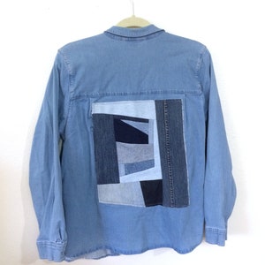 Könnte beinhalten: Ein hellblaues Jeanshemd mit einem großen Patchwork-Design auf der Rückseite. Das Patchwork besteht aus verschiedenen Blautönen von Jeansstoff.