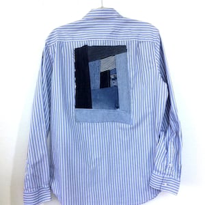 Puede incluir: Una camisa de manga larga a rayas azules y blancas con un parche de mezclilla en la espalda. El parche está hecho de diferentes piezas de mezclilla cosidas juntas en un patrón geométrico.