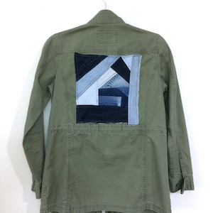 May include: A green utility jacket with a large patch on the back made of denim fabric in various shades of blue and black.