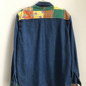 Könnte beinhalten: Ein blaues Jeanshemd mit Patchwork-Design auf der Rückseite. Das Patchwork besteht aus verschiedenen Stoffen in unterschiedlichen Farben mit floralen und geometrischen Mustern.